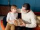 Enfant blond offrant cadeau emballé à grand-père barbu sur canapé, moment d'offrir un cadeau à son père